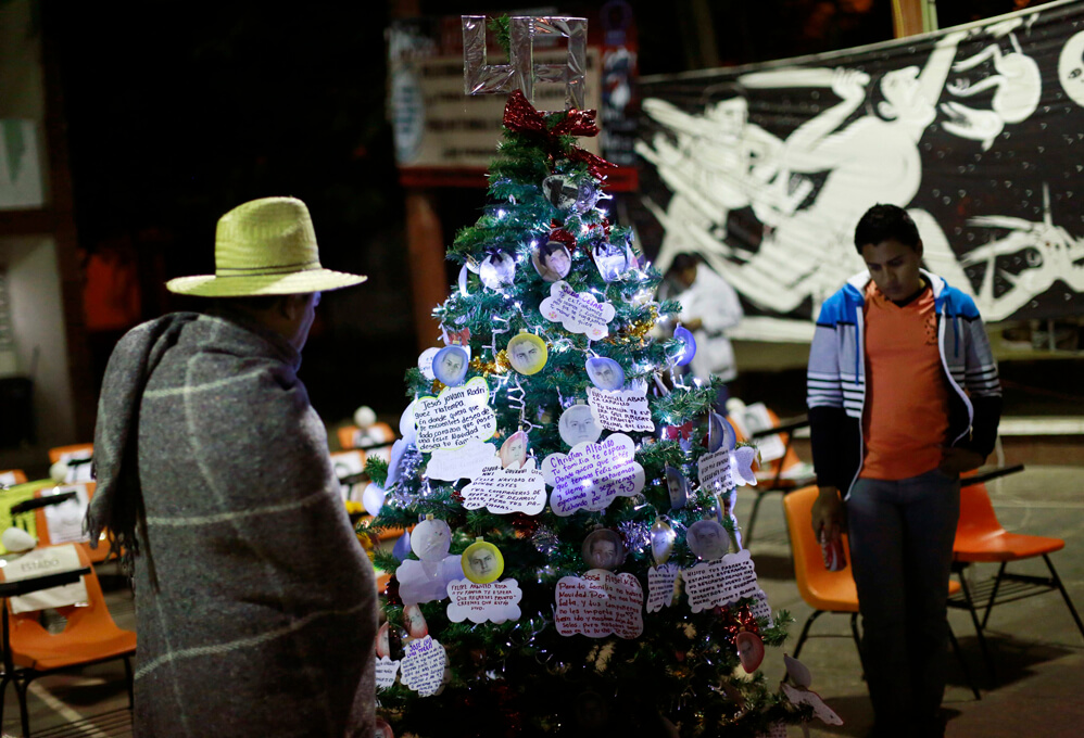 Men look at a Christmas tree, with pictures of the 43 missing trainee teachers, in the Ayotzinapa Teacher Training Raul Isidro Burgos College in Ayotzinapa, on the outskirts of Chilpancingo, Guerrero, December 24, 2014. Mexican authorities on December 7 said that mounting evidence and initial DNA tests confirmed that 43 trainee teachers who were abducted in Iguala by corrupt police on September 26 were incinerated at a garbage dump by drug gang members. 
Picture taken December 24, 2014. 
REUTERS/Jorge Dan Lopez (MEXICO - Tags: CRIME LAW EDUCATION POLITICS CIVIL UNREST SOCIETY)
