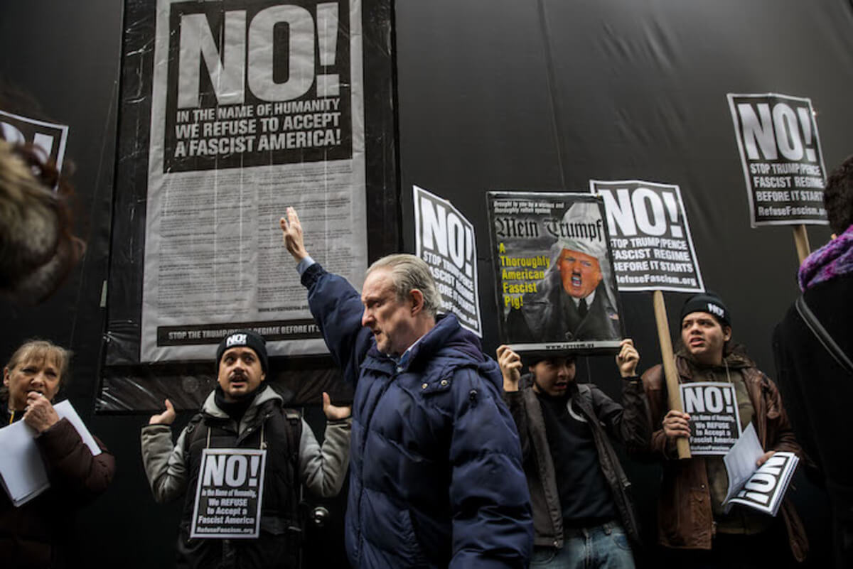 NEW YORK, NY - JANUARY 11: A man holding up his right arm walks past a small group of anti-Donald Trump across the street from Trump Tower, January 11, 2017 in New York City. On Wednesday morning, Trump is having his first press conference since winning the election.   Drew Angerer/Getty Images/AFP