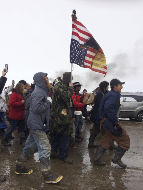 Un grupo de personas con una bandera de Estados Unidos invertida salen pacíficamente del principal campamento de protesta contra el oleoducto Dakota Access cerca de Cannon Ball, Dakota del Norte, el miércoles 22 de febrero de 2017. El Cuerpo de Ingenieros del Ejército ordenó su cierre a las 2 de la tarde del miércoles. (AP Foto/Blake Nicholson)